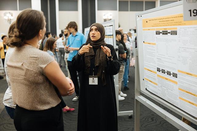 A student engages in conversation with two people in front of a poster at the Student Scholar Symposium in the Pegasus Ballroom.
