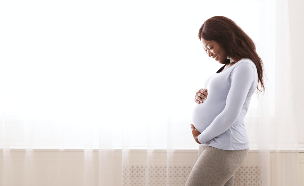 black pregnant woman hugging her tummy at home