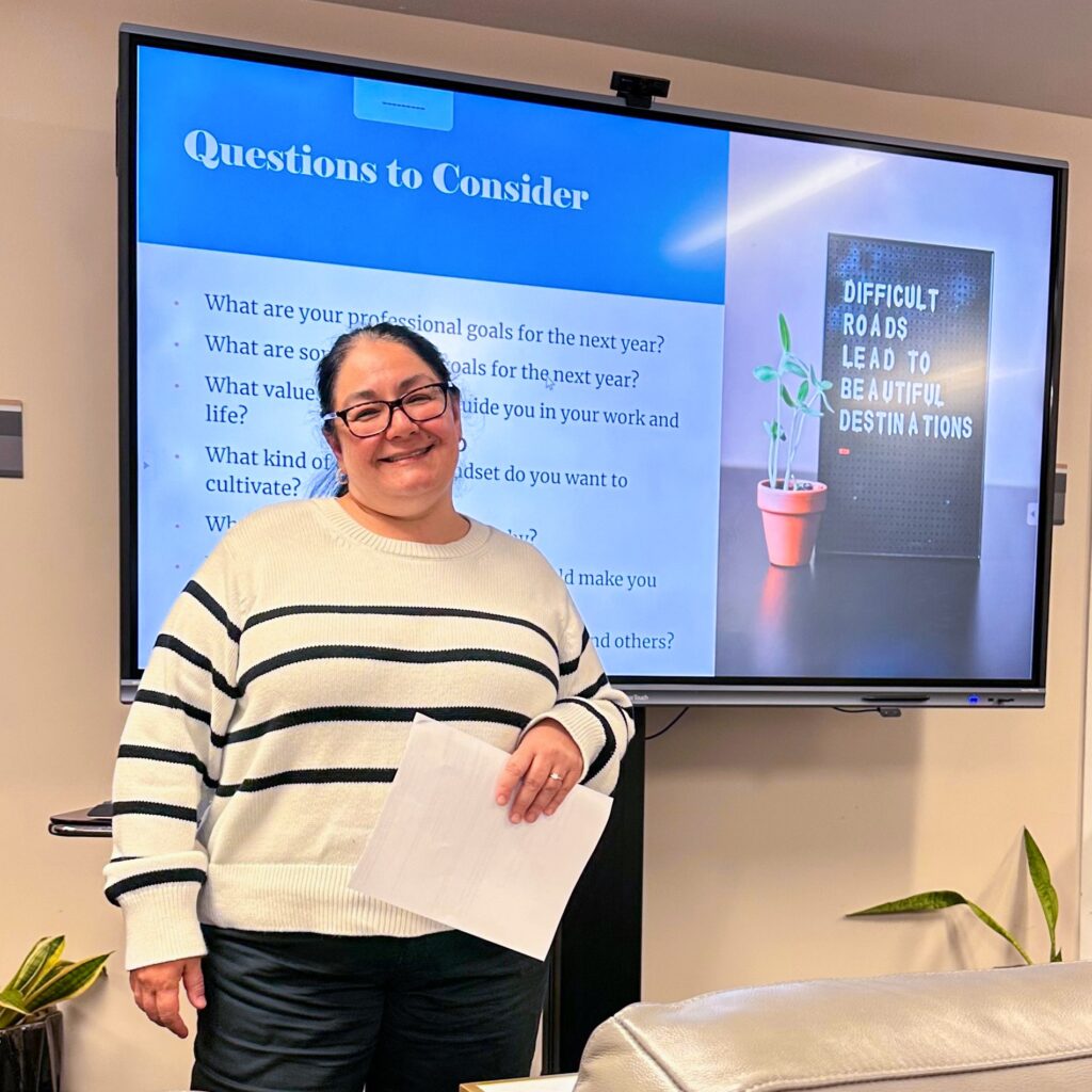Nataly Larenas facilitating a goal-setting exercise with staff at the Marriage & Family Research Institute, standing in front of a screen showing discussion questions. 