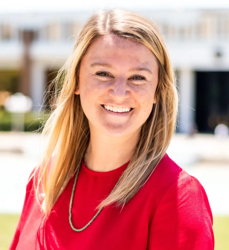 Rachel Griffin, director of New Student and Family Programs, smiles outdoors while wearing a red blouse, with a softly blurred campus setting in the background.