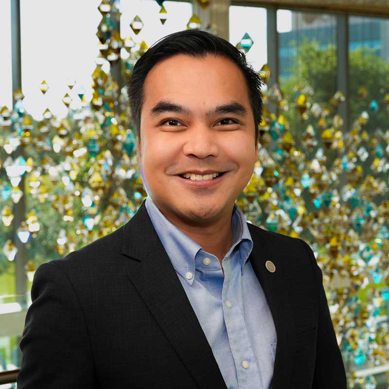 Portrait of Dr. Michael Joseph Dino of the UCF College of Nursing, smiling in front of a colorful glass art installation.