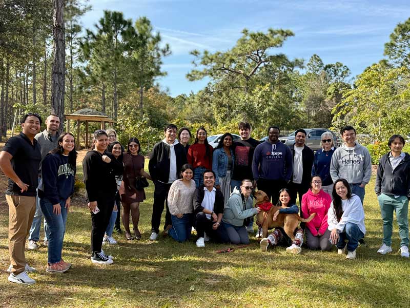 Dr. Michael Joseph Dino kneels near the center of a large group of Healthy Ageing Laboratory members gathered outdoors with two dogs.